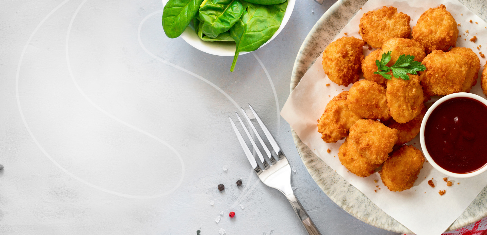 A plate of golden brown chicken nuggets with a sprig of parsley, served with a bowl of dipping sauce and a small bowl of fresh spinach. A fork and scattered peppercorns are on the light gray surface.