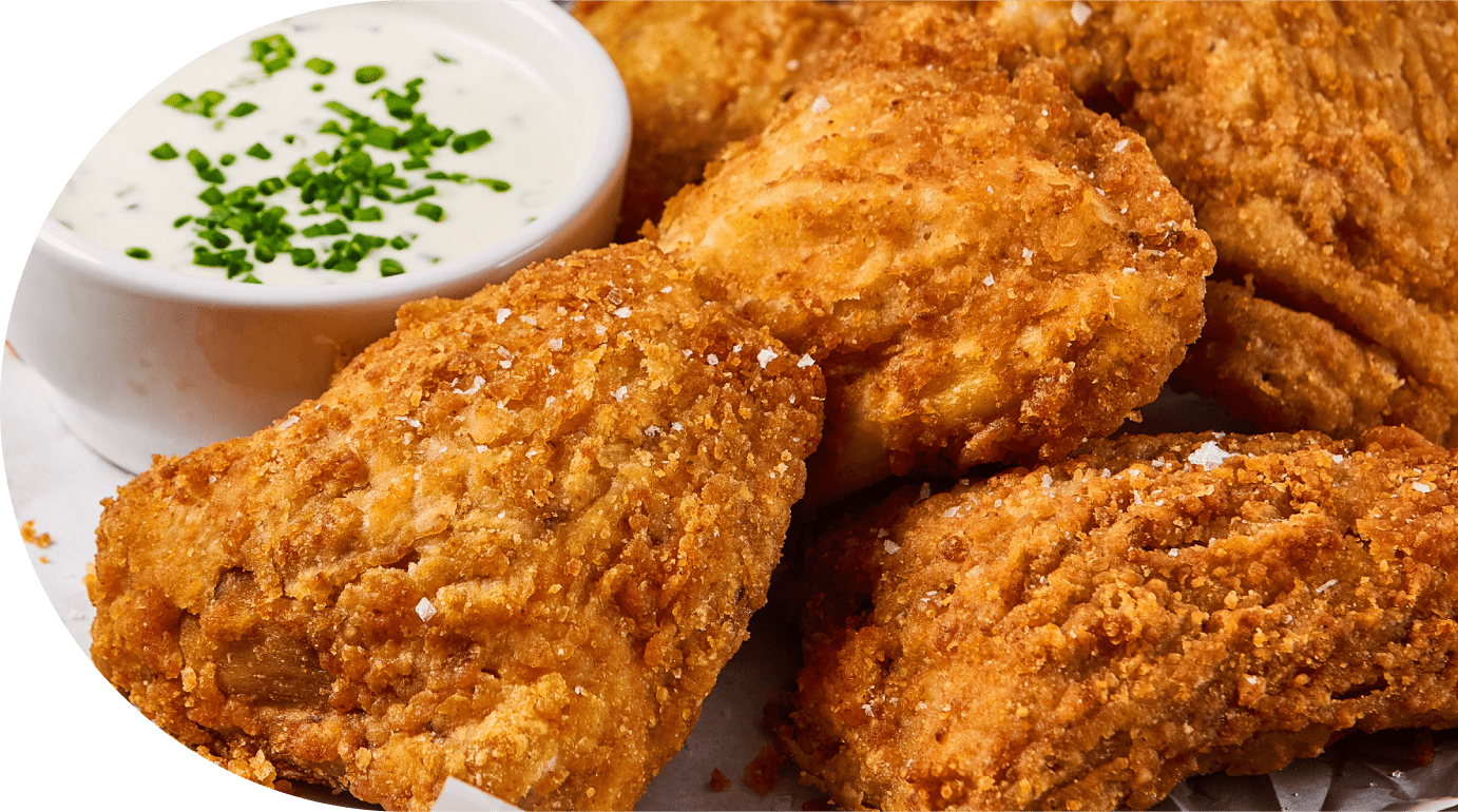 Chicken'tizers - Close-up of crispy, golden fried chicken pieces sprinkled with salt, served with a small bowl of creamy dipping sauce topped with chopped chives.