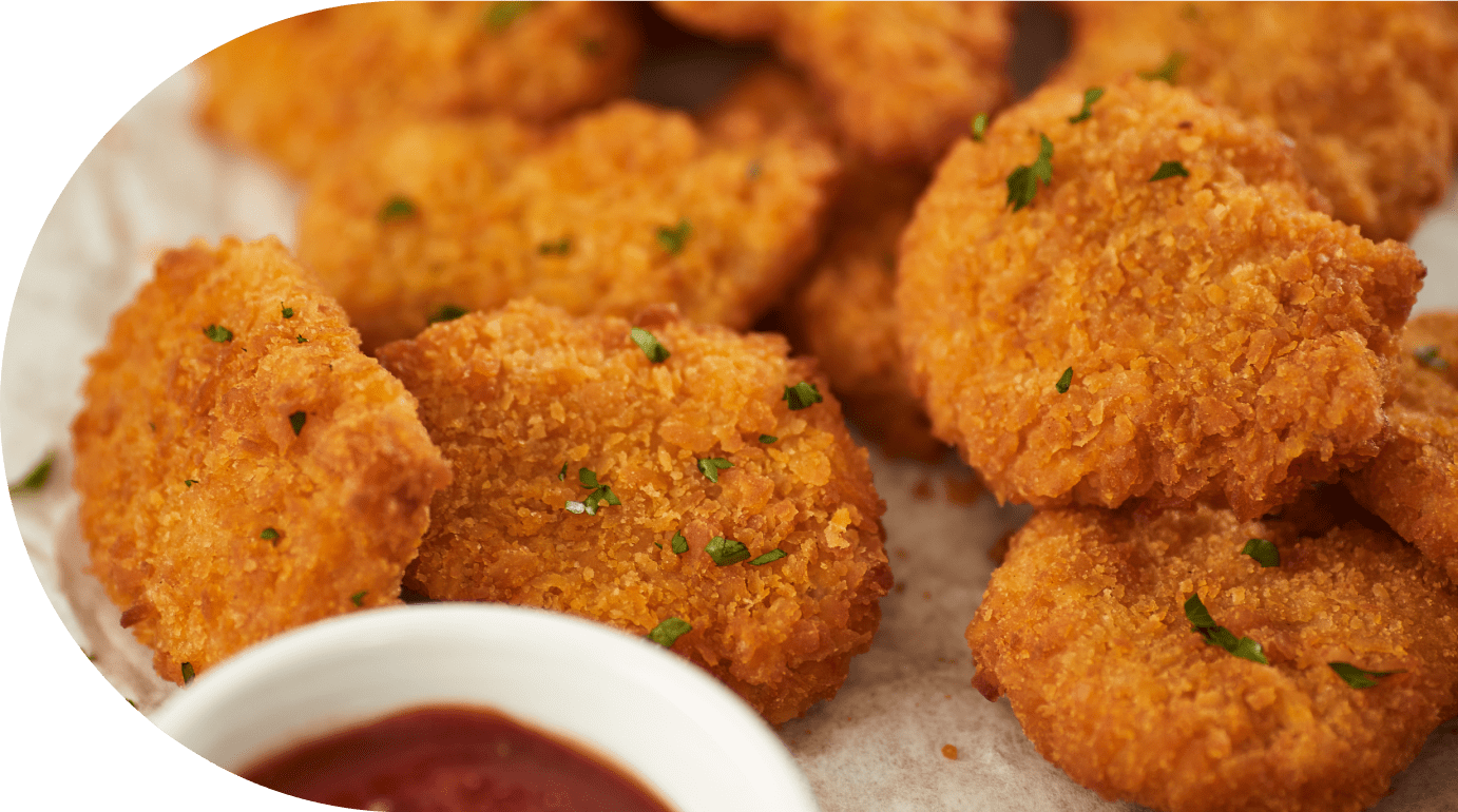 Country Range - Close-up of several golden, crispy breaded chicken nuggets garnished with small green herbs, with a dipping sauce in a white bowl nearby.