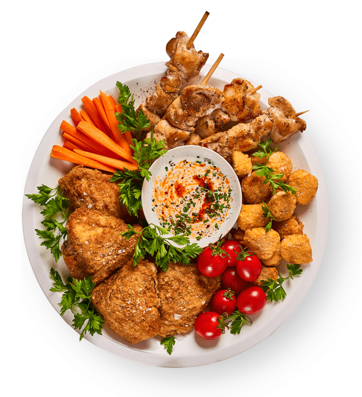 A white platter with fried chicken, chicken skewers, hush puppies, cherry tomatoes, carrot sticks, fresh parsley, and a bowl of creamy dip garnished with herbs and spices.